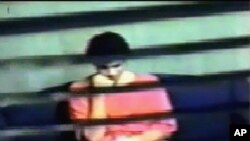 ທ້າວໂອມາຣ ຄາດຣ໌ (Omar Khadr), ເຫັນໄດ້ໃນກ້ອງວົງຈອນປິດຂອງກະຊວງປ້ອງກັນປະເທດສະຫະລັດ ພາບບັນທຶກວີດີໂອ, ນັ່ງຢູ່ໃນຫ້ອງສືບສວນ ທີ່ຄຸກໃນຄ້າຍກອງທັບເຮືອ ສະຫະລັດ ກວນທານາໂມ (Guatanamo U.S. Naval Base) ໃນຂະນະຖືກສອບຖາມໂດຍບັນດາສະມາຊິກຂອງໜ່ວຍງານດ້ານສືບລັບຂອງການາດາ.