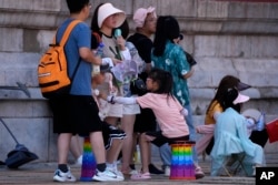 前來北京參觀故宮的遊客手持小電扇在陰涼地裡排隊等候入門。（2023年7月7日）