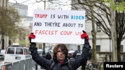 來自佛羅里達州聖奧古斯丁的阿扎雷洛2024年4月18日在特朗普接受審判的紐約法庭外舉著抗議標語，上面寫道：“特朗普和拜登是一伙的，他們將要對我們發動法西斯政變。”