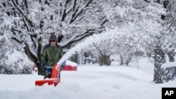 A person removes snow from a sidewalk during a winter storm in Doylestown, Pa., Feb. 13, 2024. Parts of the Northeast have been hit by a coastal storm that's dumping snow and packing strong winds in some areas.