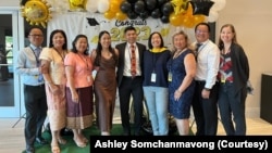 ນາງແອສລີ ສົມຈັນມະວົງ ແມ່ນຄົນທີສາມຈາກຂວາ, ນາງຢືນຄຽງຂ້າງກັບແມ່ຂອງນາງ ແລະ ຜູ້ຢູ່ທາງກາງ ແມ່ນ ປີເຕີ້ ຈິນດາວົງ, ຫົວໜ້າອົງກອນຄົນປັດຈຸບັນ.