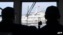 ສະມາຊິກໜ່ວຍຍາມຝັ່ງຂອງຟີລິບປິນ ສັງເກດເບິ່ງກໍາປັ່ນຍາມຝັ່ງຂອງຈີນ ທີ່ກໍາລັງຂວາງທາງພວກເຂົາເຈົ້າ ໃນລະຫວ່າງພາລະກິດຂົນສົ່ງເຄື່ອງ ໂດຍເຮືອຂົນສົ່ງພົນລະເຮືອນ ທີ່ຖືກເໝົາລໍາໂດຍກອງທັບເຮືອຟີລິບປິນ ເພື່ອນໍາສົ່ງເຄື່ອງໃຊ້ຕ່າງໆໄປສູ່ກໍາປັ່ນຂອງກອງທັບເຮືອຟີລິບປິນ ຢູ່ໃນຂົງເຂດທະເລຈີນໃຕ້ທີ່ມີຂໍ້ພິພາດກັນ.