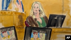ນາງ ສຕອມມີ ເດນຽລສ໌ (Stormy Daniels) ຂຶ້ນໃຫ້ການເປັນພະຍານ ໃນຂະນະທີ່ພາບໂປຣໂມດ ສຳລັບລາຍການນຶ່ງຂອງນາງ ທີ່ມີຮູບຂອງອະດີດປະທານາທິບໍດີສະຫະລັດ ທ່ານ ດໍໂນລ ທຣຳ ປາກົດຢູ່ເທິງໜ້າຈໍ ໃນສານອາຍາ ແມນຮັດຕັນ, ນະຄອນ ນິວຢອກ, ວັນທີ 9 ພຶດສະພາ 2024.