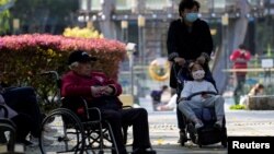 在上海一個公園裡，一名女子推著小女孩路過一位坐輪椅的老人。（2023年4月2日）