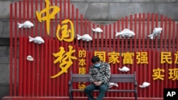 一名戴著口罩的男子在武漢街頭一個中國夢的政府宣傳牌下打盹。（2020年4月8日）