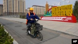 中国河北雄安街头一名工人骑车路过一处口号宣传牌 (2023年4月1日)