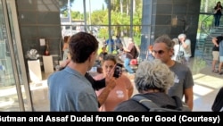 幸存者在人群中举着手机中失踪的亲人的照片。（照片受访者提供）