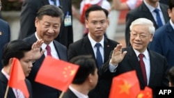 2017年11月12日，在河內舉行的歡迎儀式上，中國國家主席習近平(左)和越南共產黨總書記阮富仲(右)向舉著越南和中國國旗的學生揮手致意。（法新社照片）