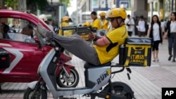 A delivery rider checks his phone as he rests on his bike outside a shopping mall in Beijing, Aug. 15, 2023. Amid high youth unemployment, some Chinese are trying to find opportunities in such sectors as food delivery and livestreaming.
