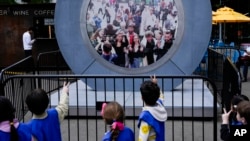 Children signal to pedestrians in Dublin, Ireland, through a livestream portal as part of an art installation on the street in New York, May 14, 2024.