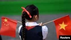 一個越南小女孩在河內的越南國會大廈前手持中越兩國國旗。（2017年11月12日）