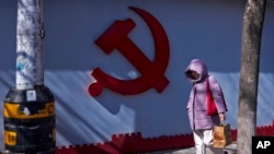 一名女子走過北京一處住宅小區圍牆上的中共標識。（2024年3月1日）