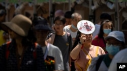 2023年6月22日，在中國正值人們慶祝端午節賽龍舟之時，然而氣溫卻熱得讓人不可思議。一位來公園觀看龍舟賽的婦女用扇子舉在頭上遮擋陽光。