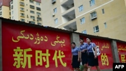 资料照：三位姑娘走过新疆莎车县街头的一幅宣传标语。（2023年7月18日）