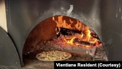 Pizza ທີ່ເປັນສູດຂອງທາງຮ້ານ, ກໍາລັງອົບຢູ່ໃນເຕົາຟືນ ເພື່ອເອົາໄປສົ່ງໃຫ້ລູກຄ້າຕາມການສັ່ງຈອງທາງອອນລາຍ.