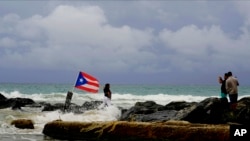 A woman poses for a photo backdropped by ocean waters and a Puerto Rican national flag, after the passing of Tropical Storm Dorian, in the Condado district of San Juan, Puerto Rico, Aug. 28, 2019. 