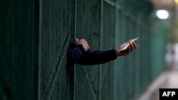 一名居民從北京潘家園一個封控小區的柵欄裡伸出握著手機的手。 （2022年4月27日）