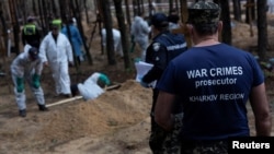 FILE - A war crimes prosecutor stands as experts work at a forest grave site during an exhumation, as Russia's attack on Ukraine continues, in the town of Izium, after its liberation by Ukrainian Armed Forces, in Ukraine's Kharkiv region, Sept. 18, 2022.