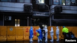 3月25日，身穿防护服的医务人员在上海一座被封闭小区的临时护墙外进行检查。