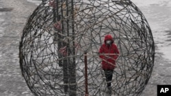 一位身着红衣戴着口罩的北京妇女正走过一个球形的编制艺术作品。中国实行的新冠病毒”清零“政策名为保护人民和经济，但实际效果可能会使中国更难摆脱疫情的肆虐。（2022年1月22日）