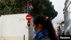 資料照片：一位女士從中國駐葡萄牙首都里斯本大使館外走過，使館牆頭伸出一個監控攝像頭，對著使館外的街區。(2022年12月21日)