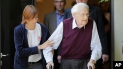 在一名红十字会工作人员的协助下，前纳粹党卫军军人奥斯卡·格罗宁（右）2015年7月15日在德国吕内堡被判决后离开法庭。