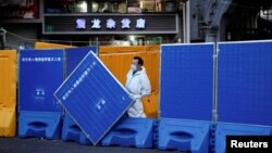 上海一名身穿防護服的工作人員站在封城使用的圍欄旁。（2022年4月11日）