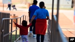 美國移民與海關執法局2018年8月9日公佈的照片顯示一名婦女手牽兒童走在德克薩斯州迪利的家庭居住中心。