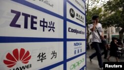 一名中國男子從武漢街頭有著華為和中興標誌的廣告牌前走過。（資料照片）