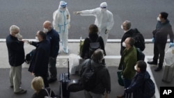 世衛組織的專家們抵達武漢天河國際機場，身穿防護服的中國工作人員給他們指方向。 （2021年1月14日）