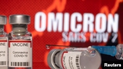资料图：在写有“奥密克戎SARS-COV-2”背景前，放置着标识为“COVID-19冠状病毒”的疫苗瓶和注射器。