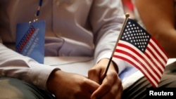 一名新公民在紐約公共圖書館的公民宣誓儀式上手持美國國旗（2018年7月3日）