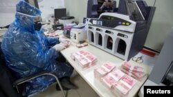 山西省太原市一名銀行工作人員身穿雨衣戴著護眼鏡和口罩點數人民幣（2020年2月24日）