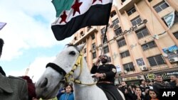 一名騎馬男子揮舞著獨立時代的敘利亞國旗，人們慶祝阿薩德政權的垮台。 (法新社：2024年12月13日)