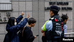 一名女子在香港西九龍裁判法院外等待根據國家安全法受到指控的47名民主活動人士的判決時打出支持的手勢。 （2024年5月30日）