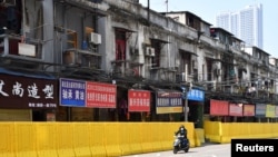 一名戴着口罩的骑车男子在武汉街头被封堵的商店旁驶过。（2020年3月5日）