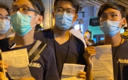 3名元朗区议员伍健伟（左起）、陈树晖、林进，7月19日下午在元朗西铁站举行7-21袭击事件一周年记者会，未开始已经被大批防暴警察包围截查，他们向记者展示警方发出的违反限聚令告票，罚款2千港币，折合约260美元 (美国之音/汤惠芸)