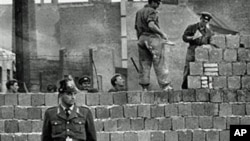 1961年10月7日,一名西柏林卫兵站在分隔东西柏林的混凝土墙前，同时，东德工人在为这道墙添砖加高。（资料照片）