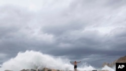 A tourist poses for a photo in front breaking waves before the expected arrival of Hurricane Lorena, in Los Cabos, Mexico, Friday, Sept. 20, 2019.