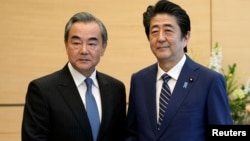 中國外長王毅在東京與日本首相安倍晉三握手。 （2019年11月25日）