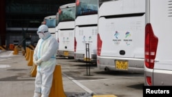 2022北京冬奧會一位身穿防護服的工作人員，他身後是專門接送冬奧會人員的大巴士。