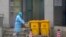 A staff member moves bio-waste containers past the entrance of the Wuhan Medical Treatment Center, where some people infected with a new virus are being treated, in Wuhan, China, Jan. 22, 2020. 