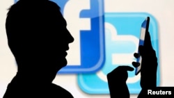 一名在脸书和推特的徽标前玩手机男子的侧影。（资料照片）