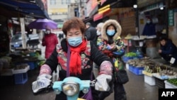 资料照片:一名戴着口罩的妇女骑着电动车穿过武汉市的一个市场。（2020年1月24日）