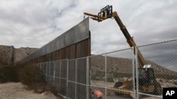  FILE - Workers raise a taller fence along the Mexico-US border between the towns of Anapra, Mexico and Sunland Park, New Mexico, Nov. 10, 2016. For almost two decades, a Mass has been celebrated there on the Day of the Dead to remember migrants who have 