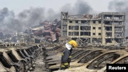 一名消防人员走过天津滨海新区被炸毁的汽车，浓烟从爆炸现场的集装箱中升起。（2015年8月14日）