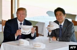 在东京附近的高尔夫球场俱乐部共进午餐时，唐纳德·川普和安倍晋三在白色球帽上签名，帽子上印着“唐纳德和晋三使同盟更伟大”（2017年11月5日）
