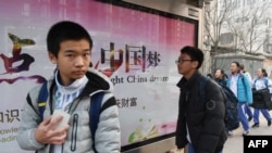 资料照片：北京一所学校外面，少年们走过宣传牌，牌上写着中英文口号“点亮中国梦 知识改变命运 付出收获财富”。(2018年3月12日)