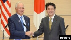 日本首相安倍晉三（右）在東盟高峰會上與與會的馬來西亞外長納吉（左）握手。