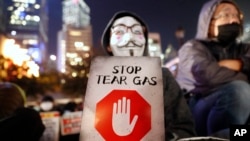 一名香港示威者手舉標語牌抗議港警使用催淚彈。 （2019年12月6日）